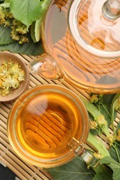 Photo of Tasty linden tea in cup, teapot, leaves and flowers on bamboo mat, flat lay