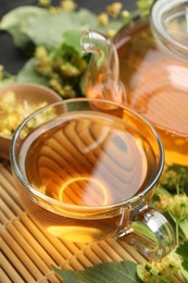 Photo of Tasty linden tea in cup, teapot, leaves and flowers on table, closeup