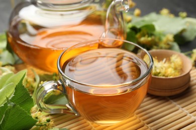Photo of Tasty linden tea in cup, teapot, leaves and flowers on table, closeup