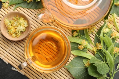 Photo of Tasty linden tea in cup, teapot, leaves and flowers on dark table, top view