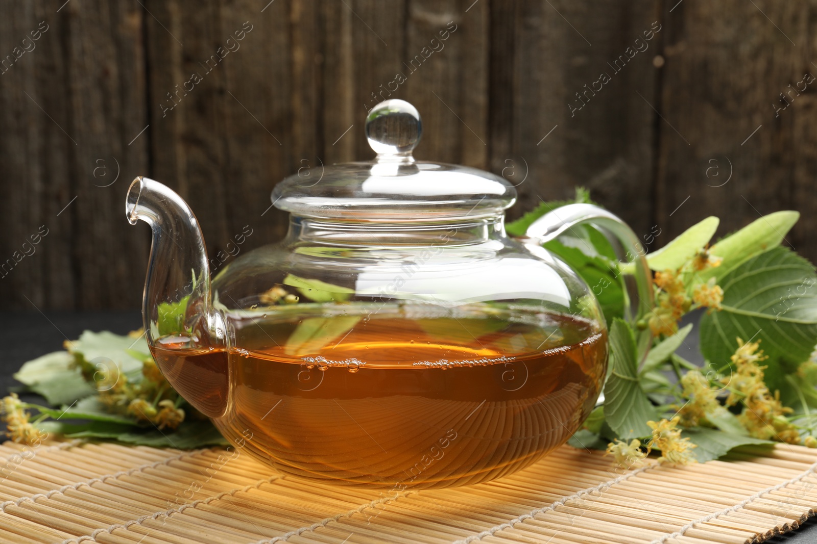 Tasty linden tea in teapot, leaves and flowers on table against wooden background, closeup Photo of Tasty linden tea in teapot, leaves and flowers on table against wooden background, closeup