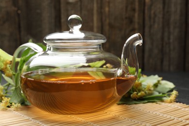 Photo of Tasty linden tea in teapot, leaves and flowers on table against wooden background, closeup
