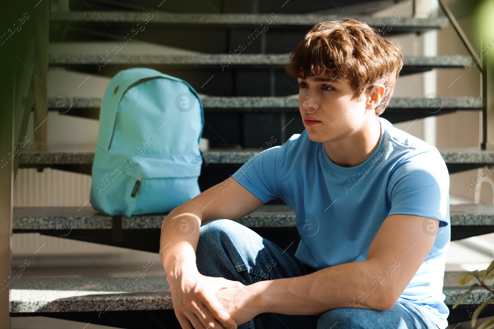 Teen problems. Upset teenage boy on stairs indoors Photo of Teen problems. Upset teenage boy on stairs indoors
