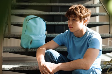 Photo of Teen problems. Upset teenage boy on stairs indoors
