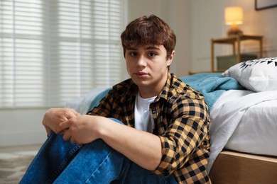 Photo of Teen problems. Upset teenage boy near bed at home