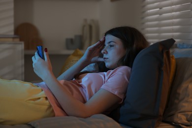 Photo of Upset teenage girl with smartphone on bed at night