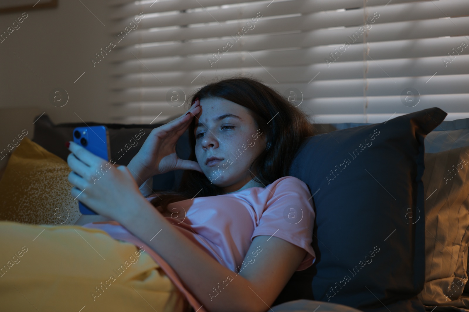 Upset teenage girl with smartphone on bed at night Photo of Upset teenage girl with smartphone on bed at night