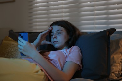 Photo of Upset teenage girl with smartphone on bed at night