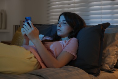 Photo of Upset teenage girl with smartphone on bed at night