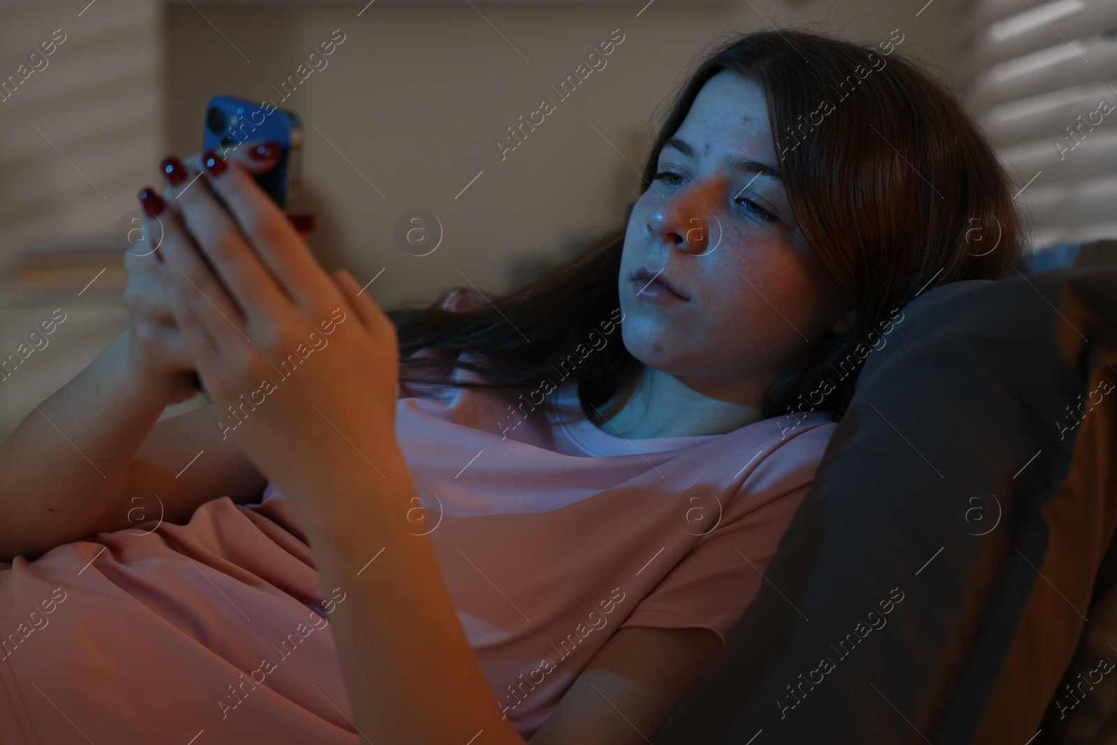 Upset teenage girl with smartphone on bed at night Photo of Upset teenage girl with smartphone on bed at night