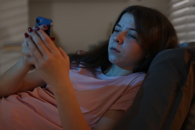 Photo of Upset teenage girl with smartphone on bed at night