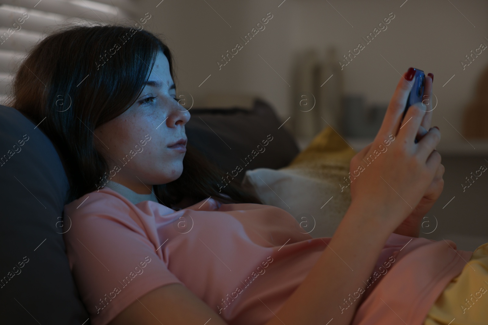 Upset teenage girl with smartphone on bed at night Photo of Upset teenage girl with smartphone on bed at night