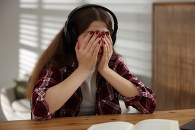 Photo of Stressed teenage girl studying at desk indoors