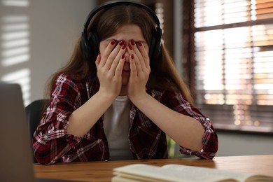 Photo of Stressed teenage girl studying at desk indoors