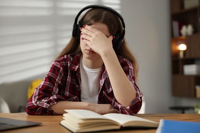 Photo of Stressed teenage girl studying at desk indoors