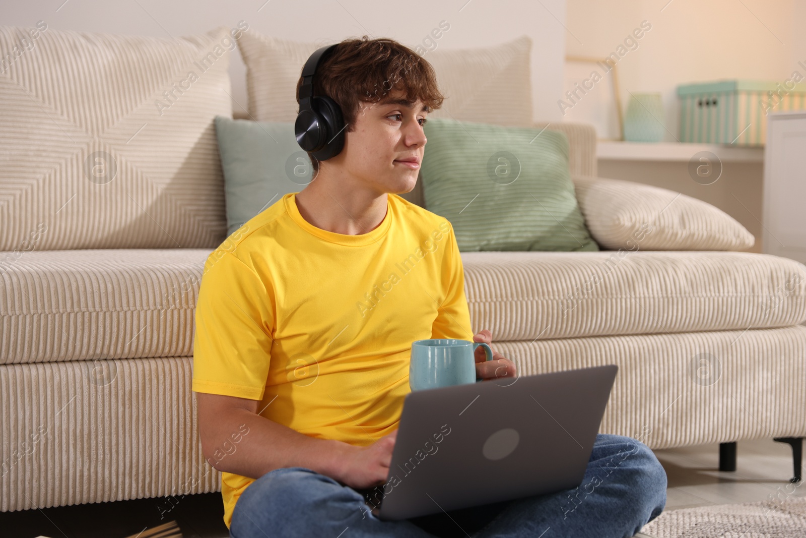 Teenage student with cup of drink using laptop while studying on floor at home Photo of Teenage student with cup of drink using laptop while studying on floor at home
