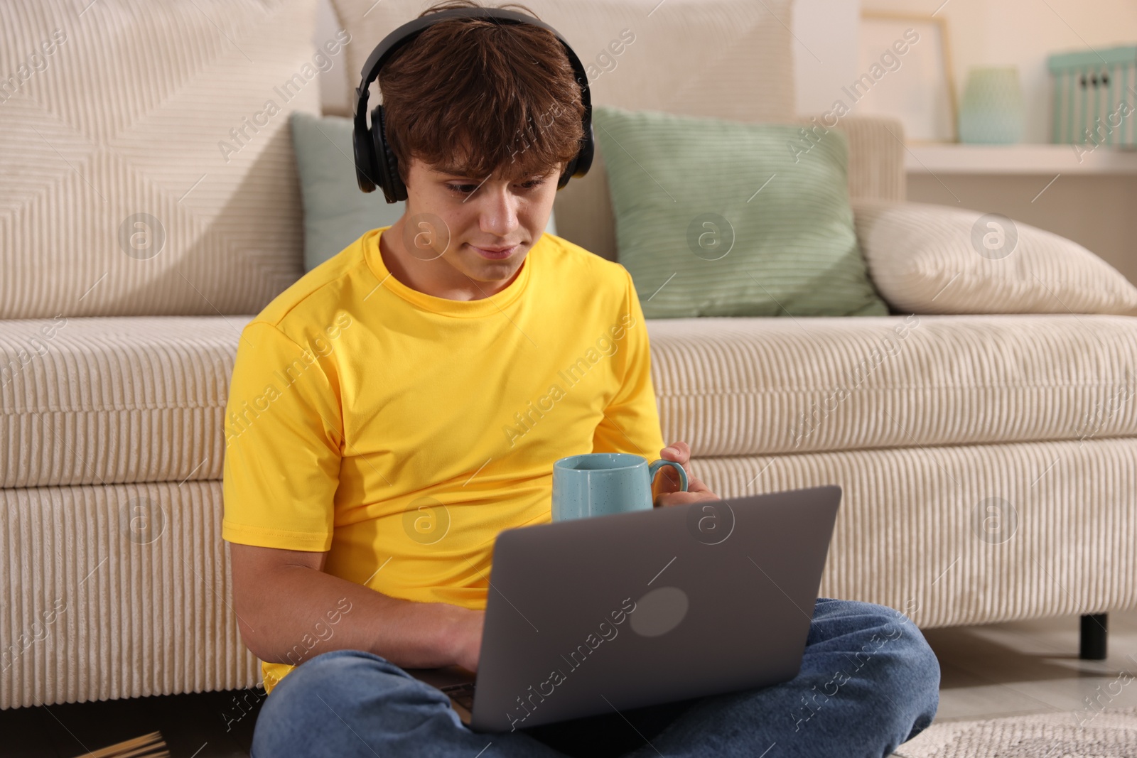 Teenage student with cup of drink using laptop while studying on floor at home Photo of Teenage student with cup of drink using laptop while studying on floor at home