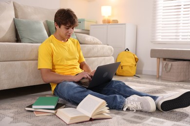 Photo of Teenage student using laptop while studying on floor at home