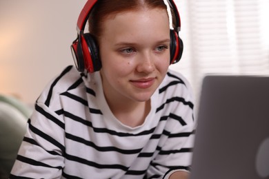 Photo of Teenage student in headphones using laptop while studying at home