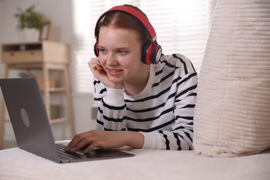 Photo of Teenage student in headphones using laptop while studying on sofa at home