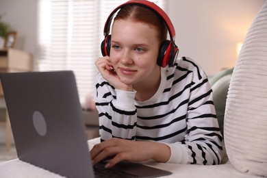 Photo of Teenage student in headphones using laptop while studying on sofa at home