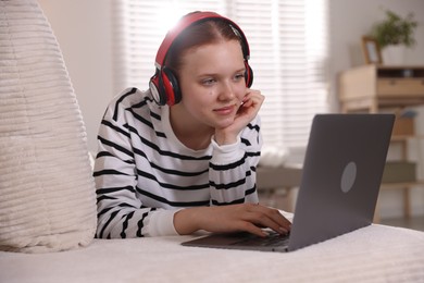 Photo of Teenage student in headphones using laptop while studying on sofa at home