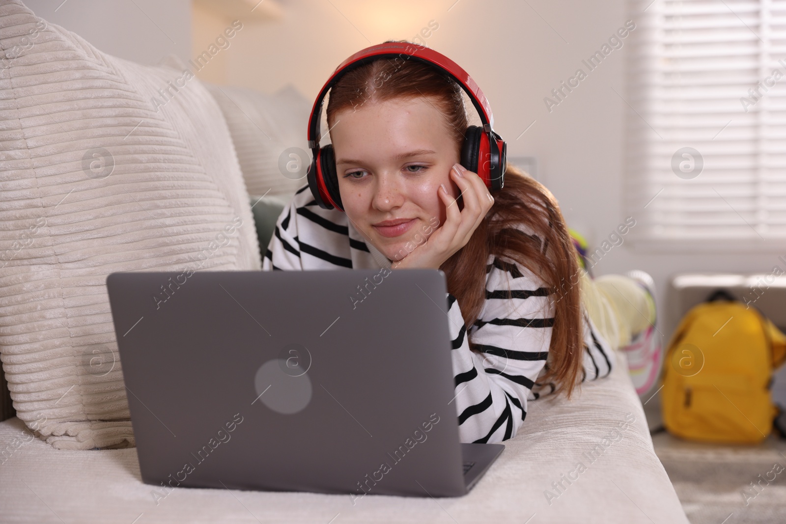 Teenage student in headphones using laptop while studying on sofa at home Photo of Teenage student in headphones using laptop while studying on sofa at home