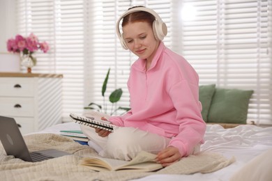 Photo of Teenage student in headphones studying on bed at home