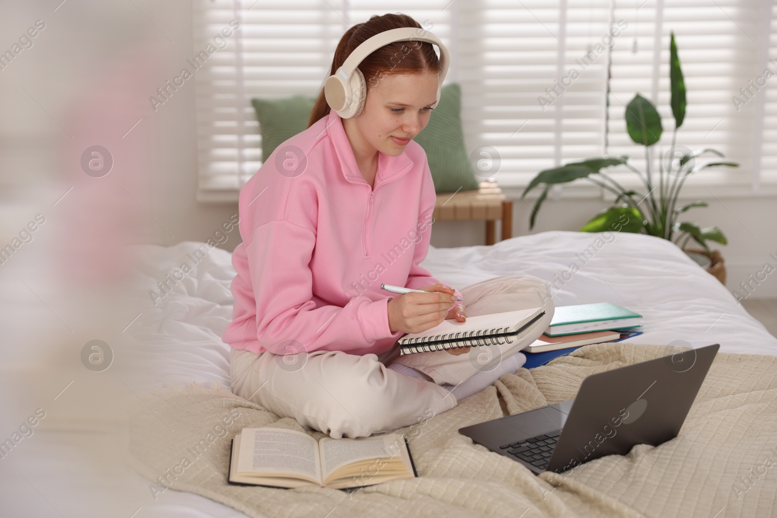 Teenage student in headphones studying on bed at home Photo of Teenage student in headphones studying on bed at home