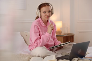 Photo of Teenage student in headphones studying on bed at home