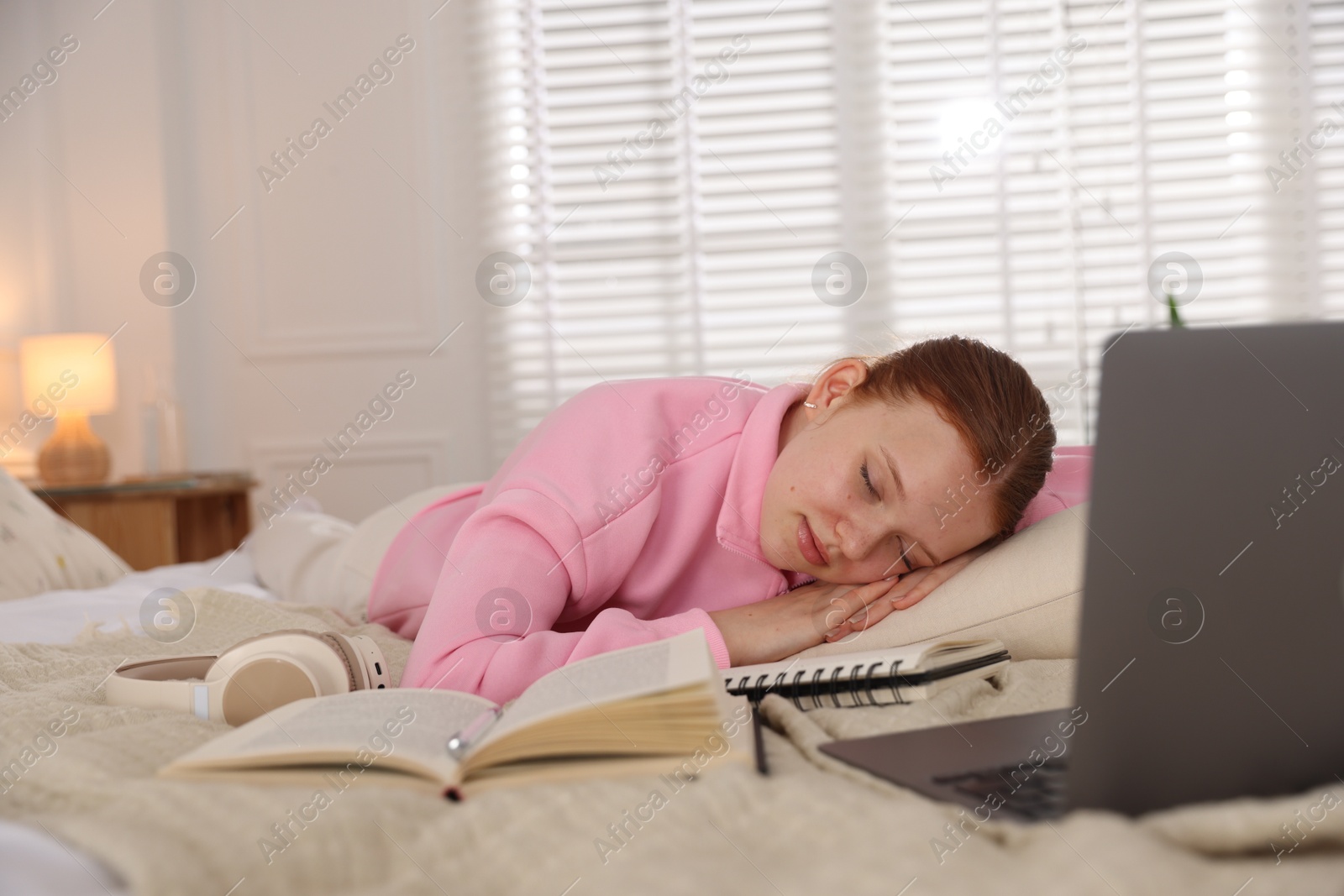 Tired teenage student sleeping near books and laptop on bed at home Photo of Tired teenage student sleeping near books and laptop on bed at home