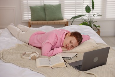 Photo of Tired teenage student sleeping near books and laptop on bed at home