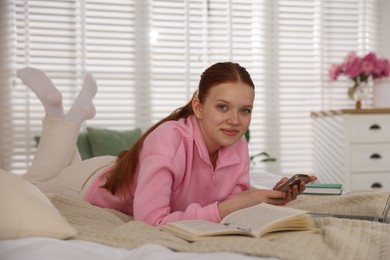 Photo of Teenage student using smartphone while studying on bed at home