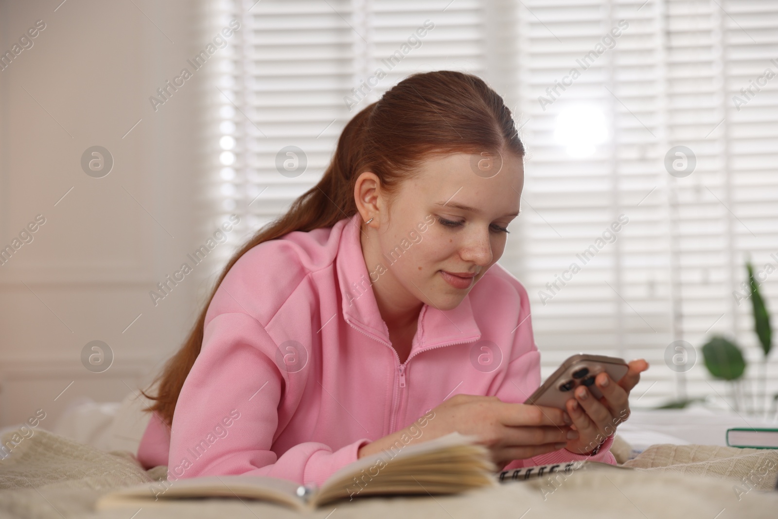 Teenage student using smartphone while studying on bed at home Photo of Teenage student using smartphone while studying on bed at home