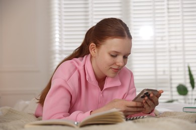Photo of Teenage student using smartphone while studying on bed at home