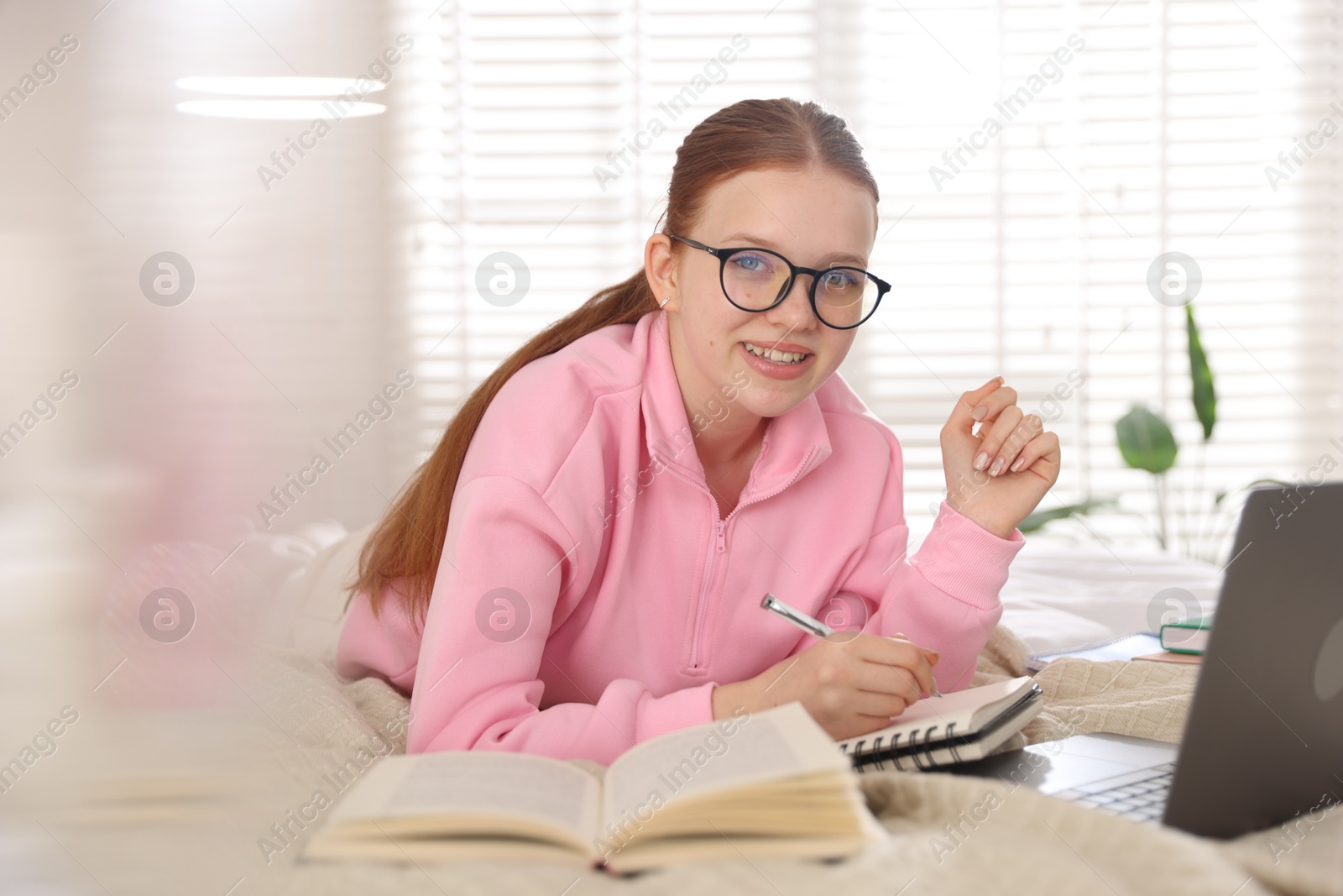 Teenage student taking notes while studying near laptop on bed at home Photo of Teenage student taking notes while studying near laptop on bed at home