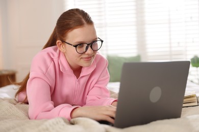 Photo of Teenage student in glasses using laptop while studying on bed at home