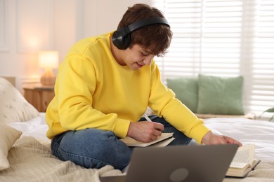Photo of Teenage student in headphones studying on bed at home