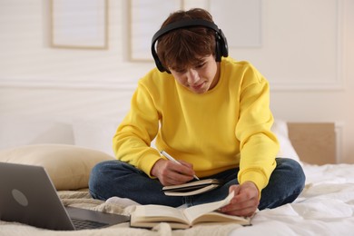 Photo of Teenage student in headphones studying on bed at home