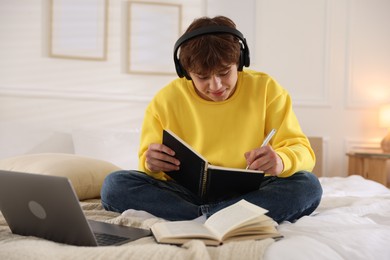 Photo of Teenage student in headphones studying on bed at home