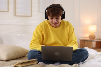 Photo of Teenage student in headphones using laptop while studying on bed at home