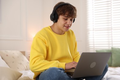 Photo of Teenage student in headphones using laptop while studying on bed at home