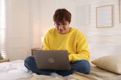 Photo of Teenage student in glasses using laptop while studying on bed at home