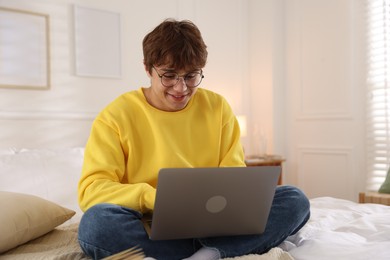 Photo of Teenage student in glasses using laptop while studying on bed at home