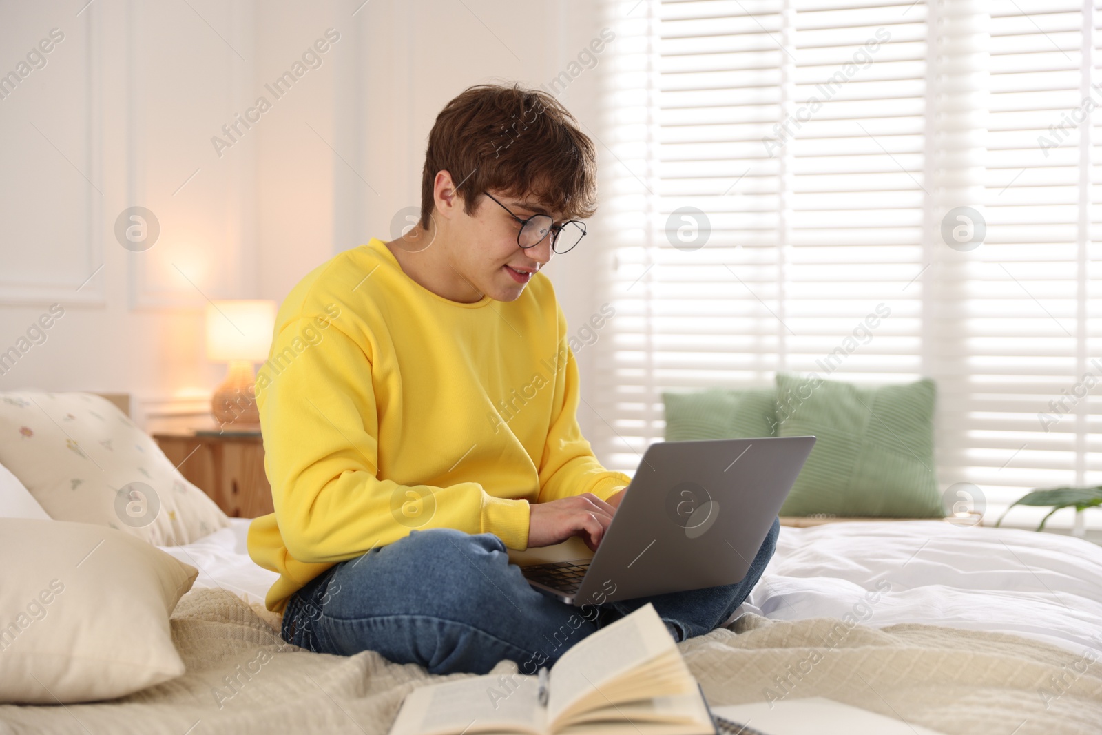 Teenage student in glasses using laptop while studying on bed at home Photo of Teenage student in glasses using laptop while studying on bed at home