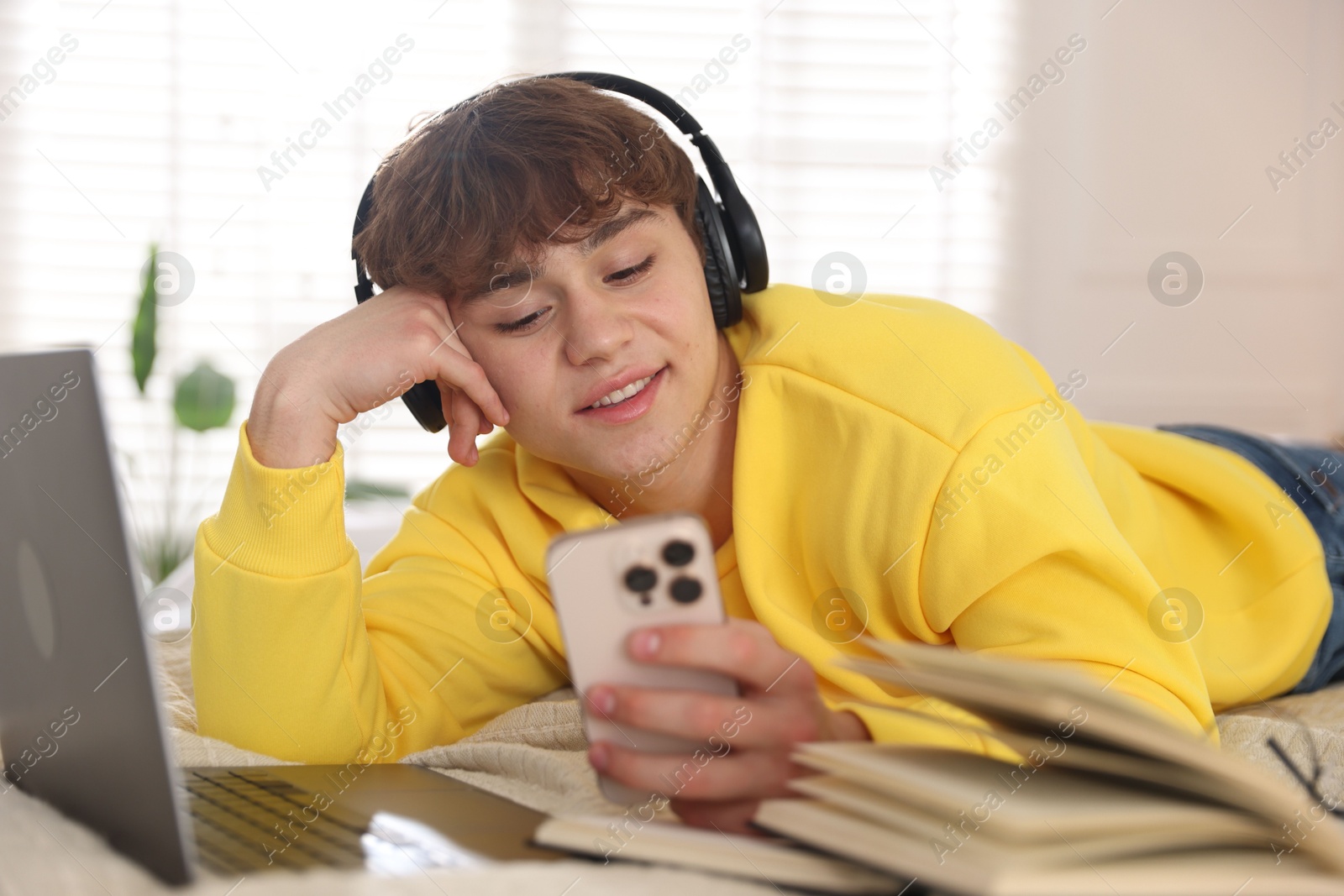 Teenage student in headphones using smartphone while studying on bed at home Photo of Teenage student in headphones using smartphone while studying on bed at home