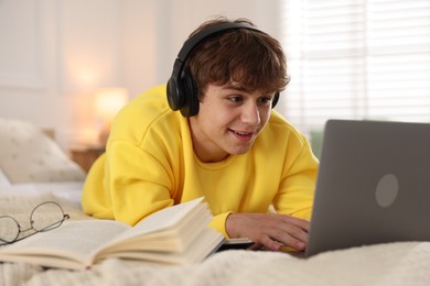 Photo of Teenage student using laptop while studying on bed at home