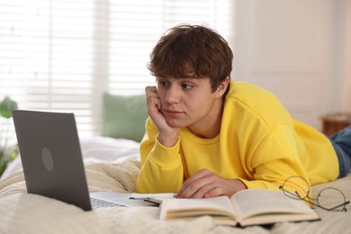 Photo of Teenage student using laptop while studying on bed at home