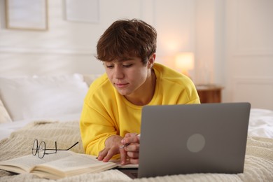 Photo of Teenage student taking notes while studying near laptop on bed at home