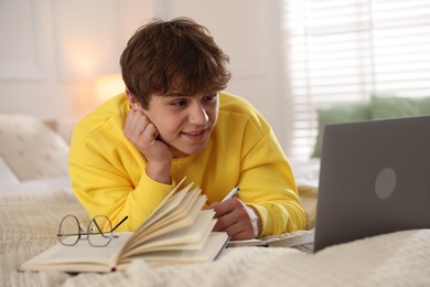 Photo of Teenage student taking notes while studying near laptop on bed at home